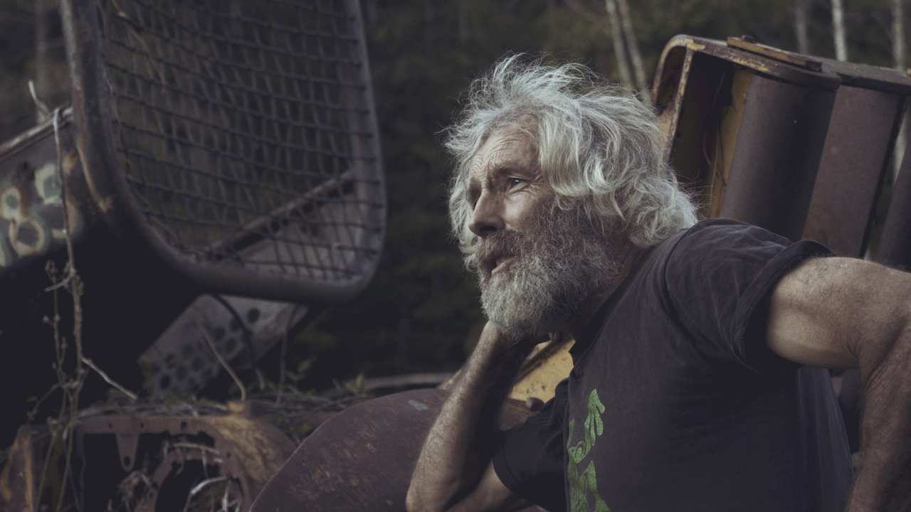 a man with a beard leaning on farm equipment